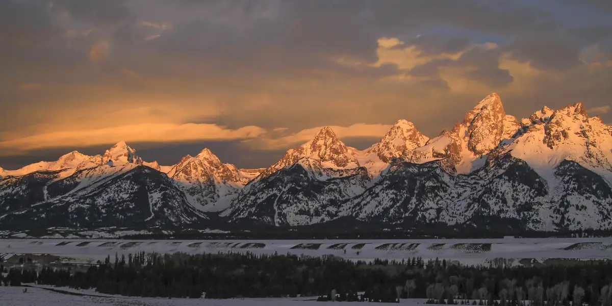 Sunrise light on the snow-capped Teton Range above a forested valley in Grand Teton National Park, Wyoming
