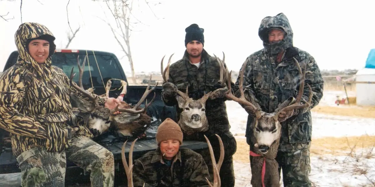 Four hunters in camouflage kneeling with their mule deer bucks at Charles M. Russell National Wildlife Refuge, Montana